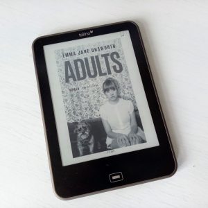 Ein Reader zeigt das Cover von "Adults" mit einer unglücklichen jungen Frau neben einem Hund vor einer Tapete