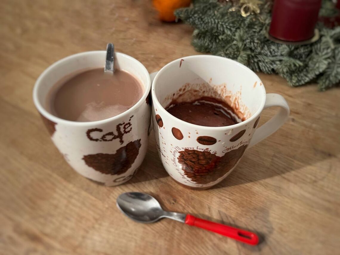 Zwei Tassen stehen auf einem Holztisch, in einer Tasse ist Kaffee, in der zweiten Tasse ist ein Schoko-Tassenkuchen