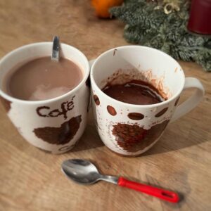 Zwei Tassen stehen auf einem Holztisch, in einer Tasse ist Kaffee, in der zweiten Tasse ist ein Schoko-Tassenkuchen